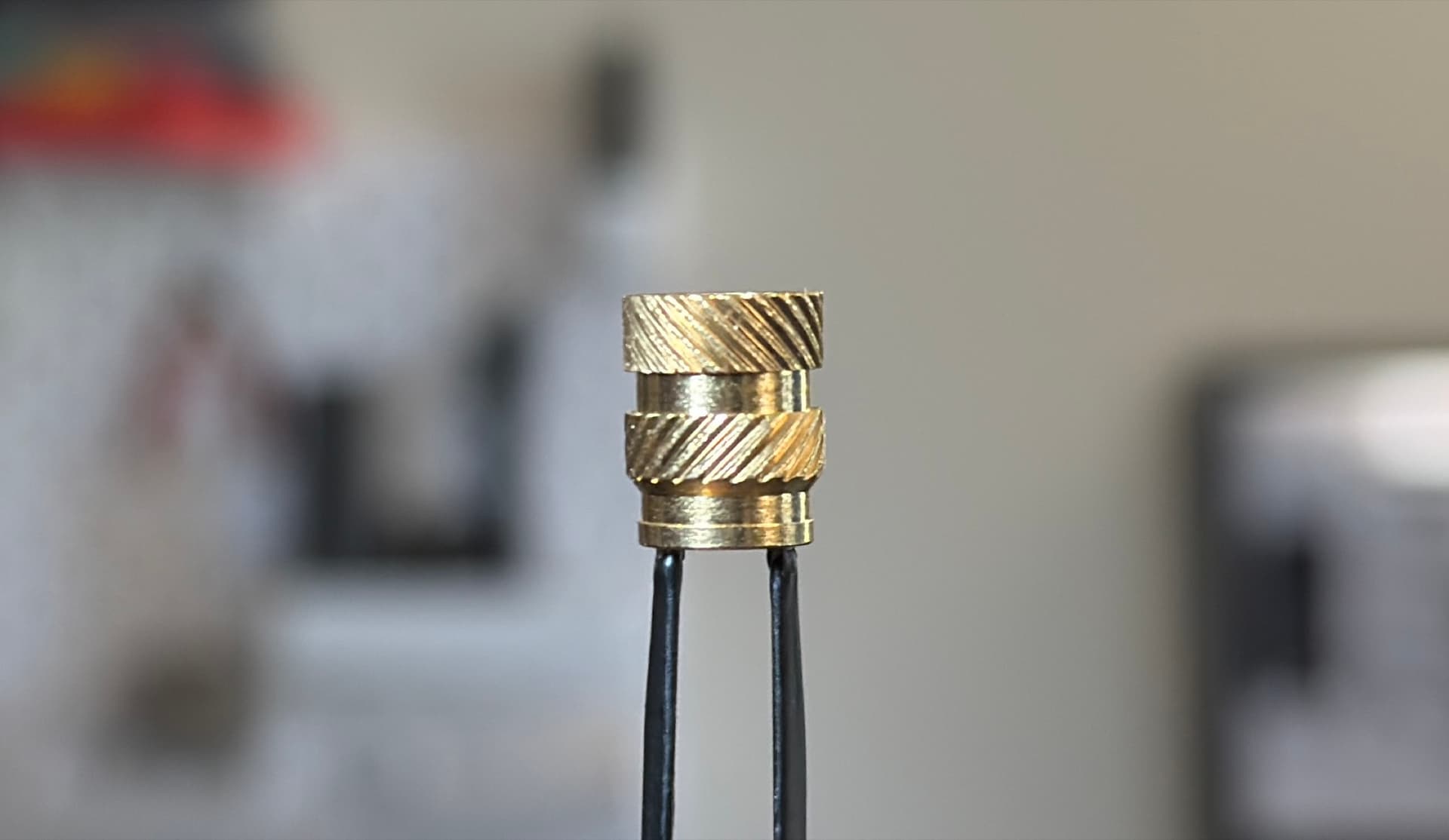 Close-up of a brass heat-set insert showing the stepped pilot and opposing knurl bands