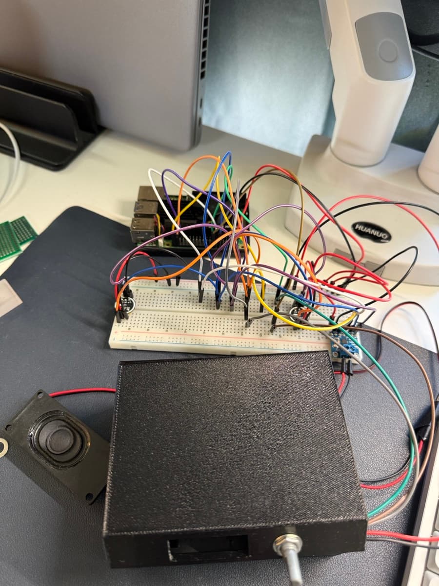 A smart speaker prototype sits on a desk next to various electronic components and tools.
